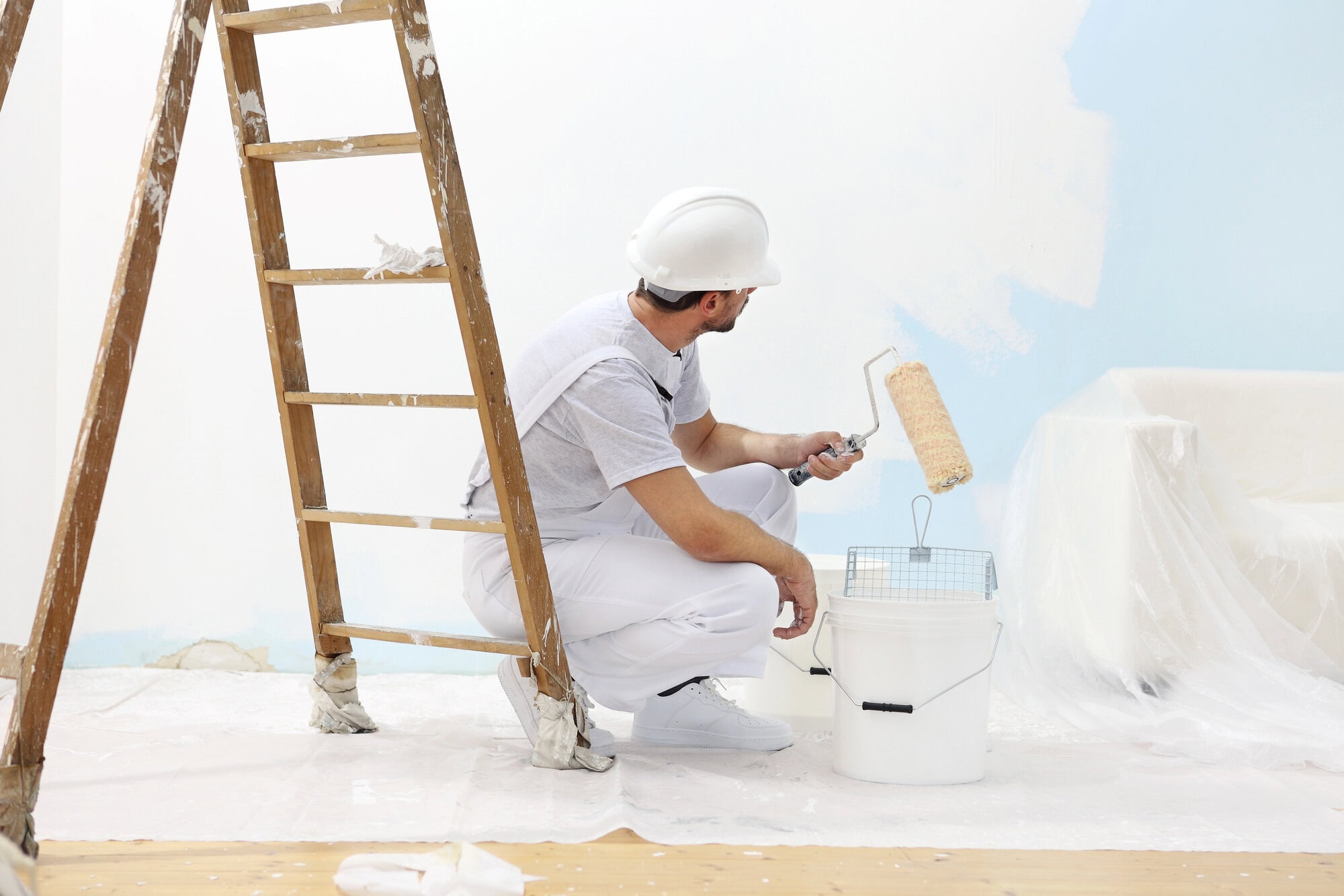 Painter man at work takes the color with paint roller from bucket
